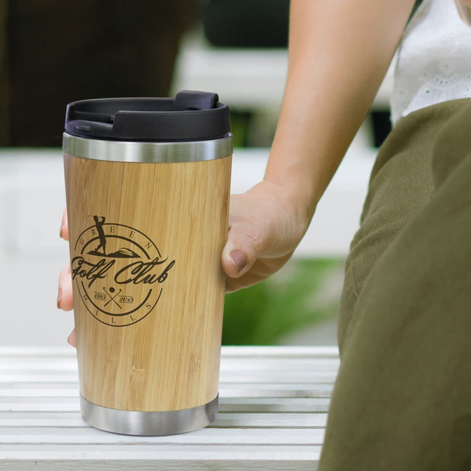 A bamboo double wall cup with a stainless steel base, featuring a logo and held in a person's hand.