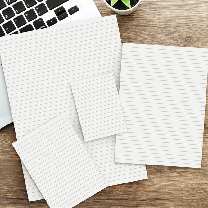 A collection of lined note pads in various sizes, featuring a light colour scheme, on a wooden desk beside a laptop.