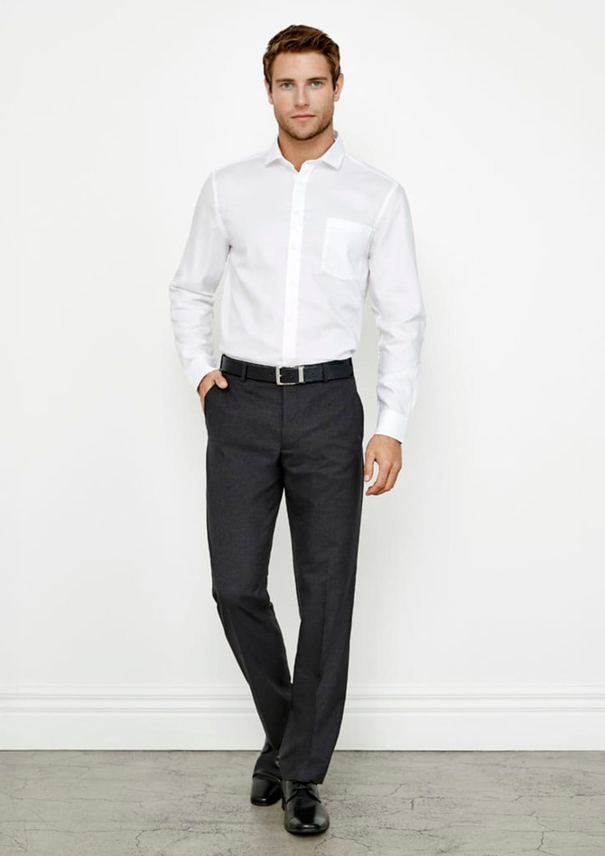 A man poses in a white shirt and dark grey classic flat pants, with a belt and sleek shoes, against a plain background.