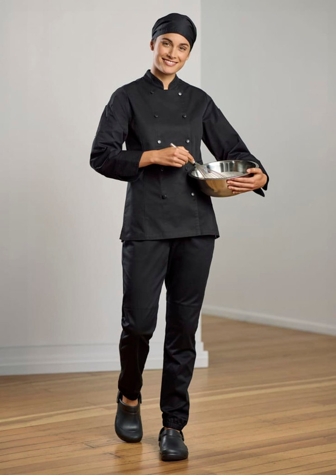 A woman wearing a black long sleeve chef jacket and pants, holding a mixing bowl in a kitchen setting.
