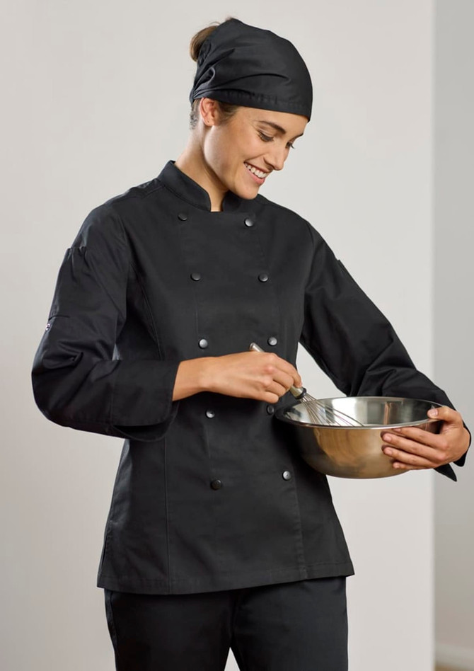 A woman in a black long sleeve chef jacket and matching headband, whisking in a stainless steel bowl.
