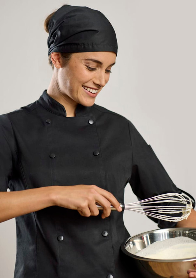 A chef in a black long sleeve jacket and matching headscarf is whisking ingredients in a bowl.
