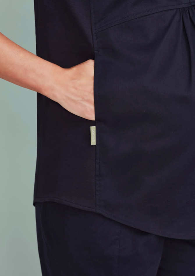 A navy women's scrub tunic top featuring a side pocket and a simple design. It includes a branding logo.