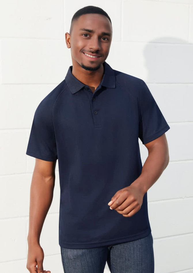 A navy short sleeve polo shirt with a collar and a logo, worn by a smiling man against a white wall.
