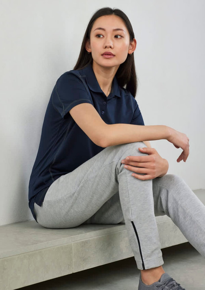 A navy women's short sleeve polo shirt, worn with grey sweatpants, displayed in a casual setting. It features a logo.