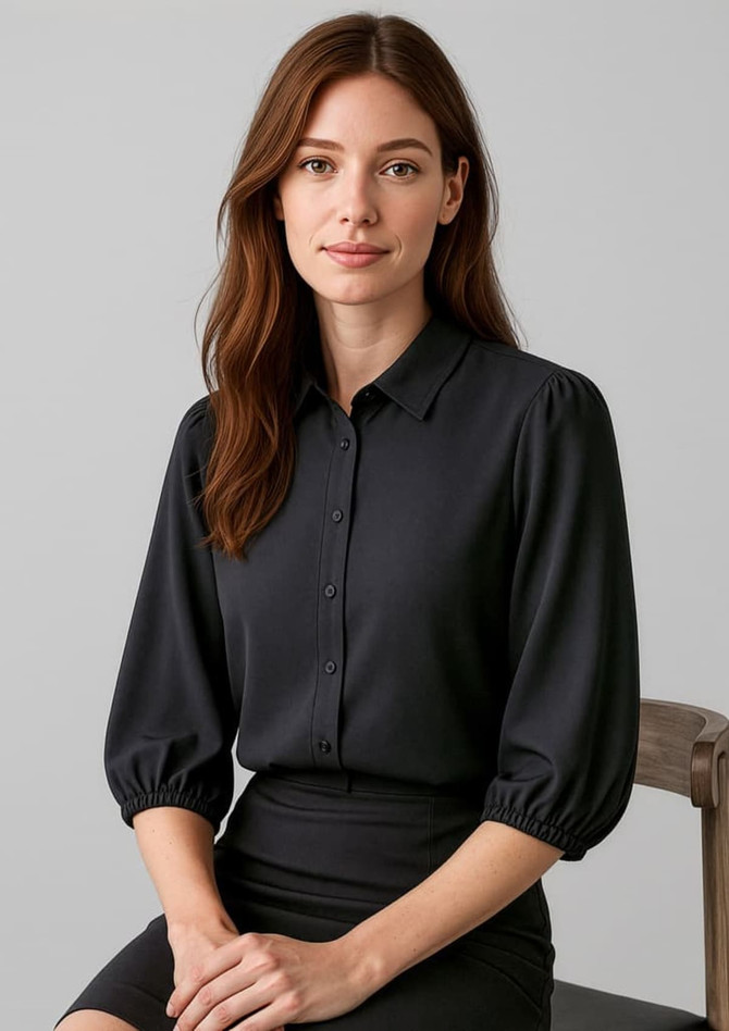 A black 3/4 sleeve blouse with a button-down front and rounded sleeves, worn by a model seated on a chair.