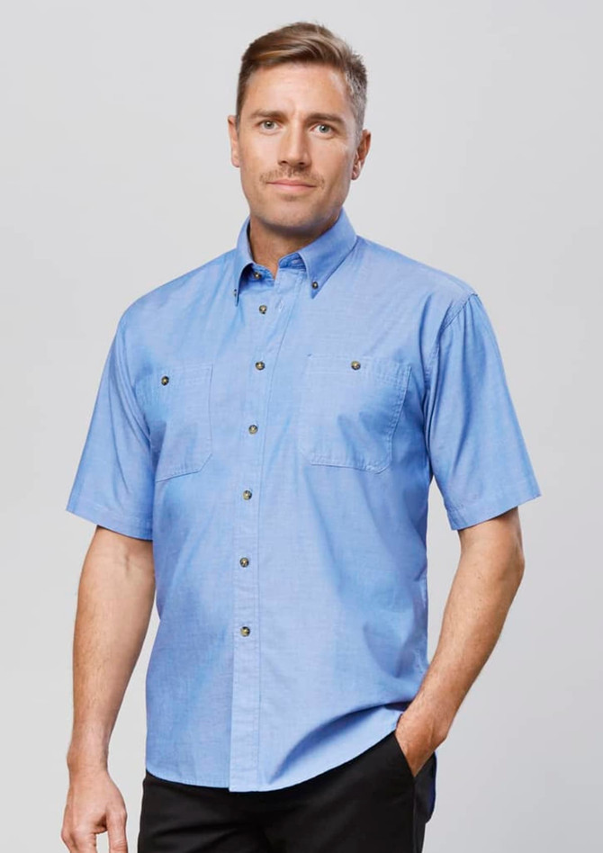 A blue chambray short-sleeve button-up shirt with two front pockets and a logo on the chest.
