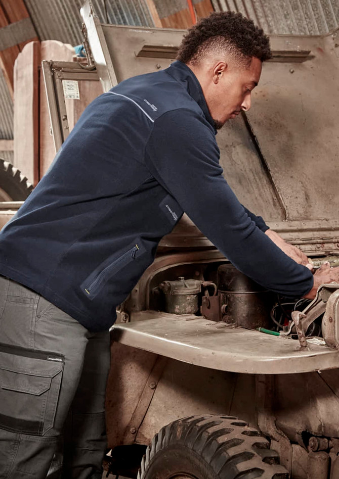 A person wearing a navy lightweight 1/4 zip polar fleece working on a vehicle under the hood, featuring a logo.