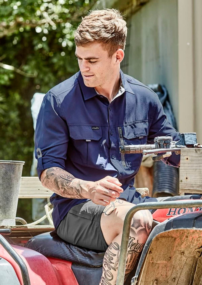 A man wearing a navy long sleeve button-up shirt sits on an all-terrain vehicle, surrounded by greenery.