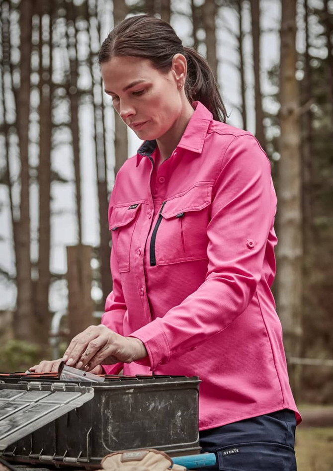 A long sleeve women's button-up shirt in pink, featuring chest pockets, worn outdoors among trees.