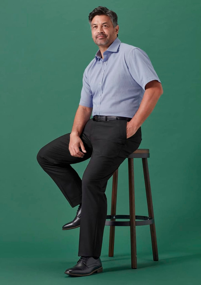Men's straight leg pants in black, worn by a model seated on a stool. The model is dressed in a blue shirt and black shoes.