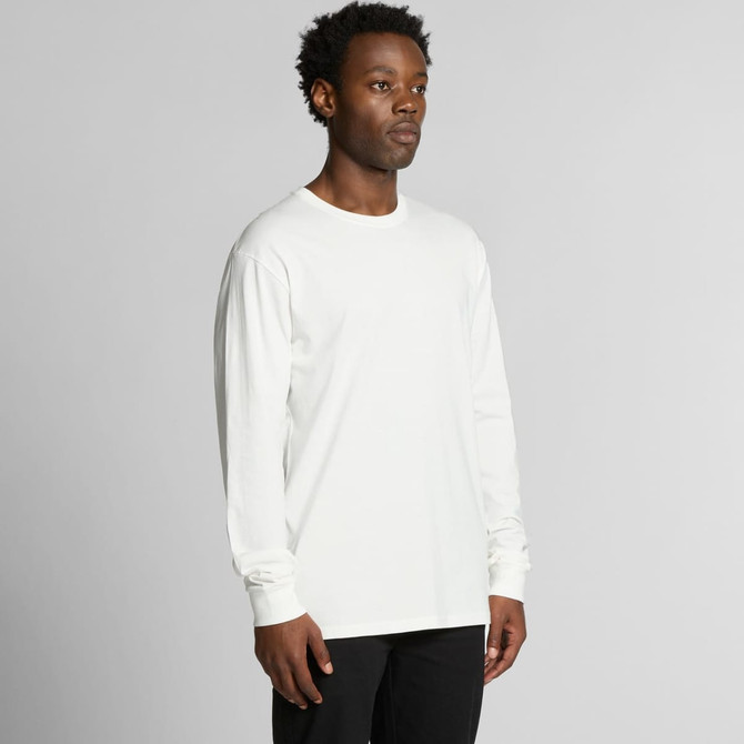 A man wearing a long-sleeve white t-shirt, standing against a plain background. The shirt features a logo.
