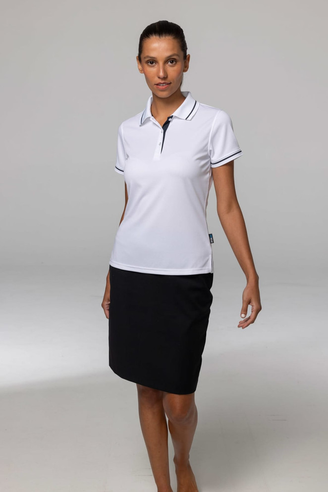 A woman is wearing a white polo shirt paired with a black skirt, standing on a neutral background. The polo has a logo.