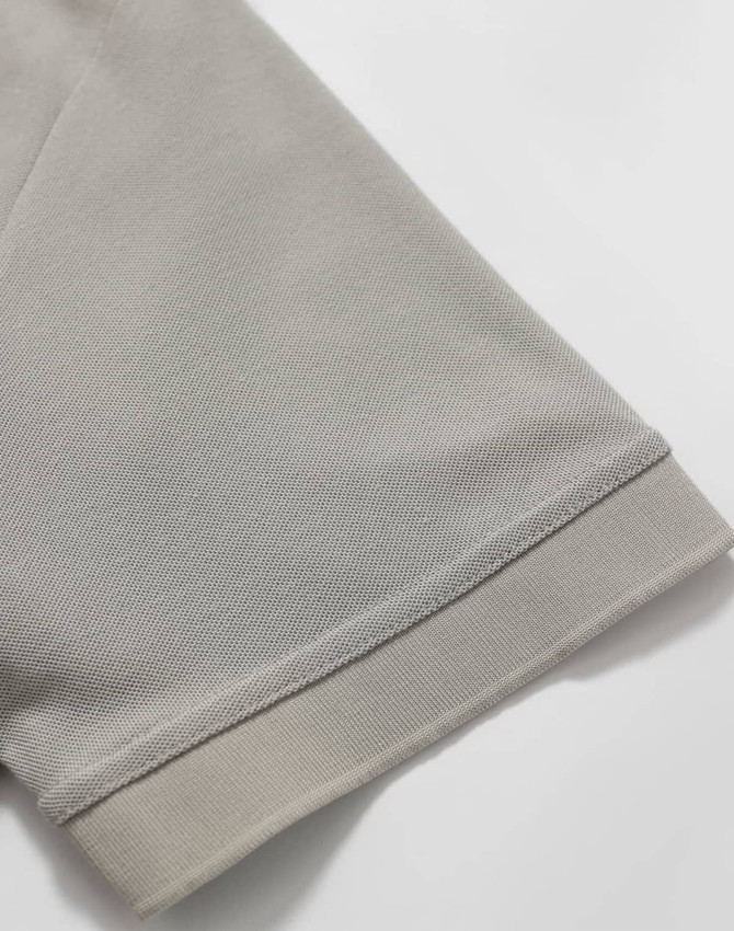A close-up of a light grey polo shirt sleeve, featuring a solid hem and a smooth fabric texture.