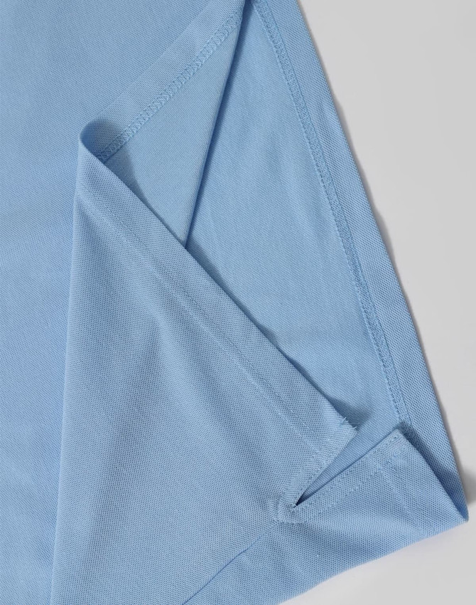 A light blue polo shirt featuring a folded sleeve, with a subtle branding logo.