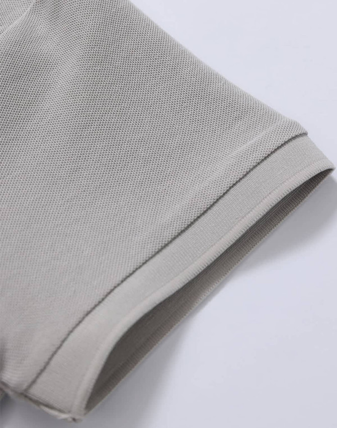 A close-up of a light grey polo shirt's sleeve, showcasing the pique texture and stitch detailing.