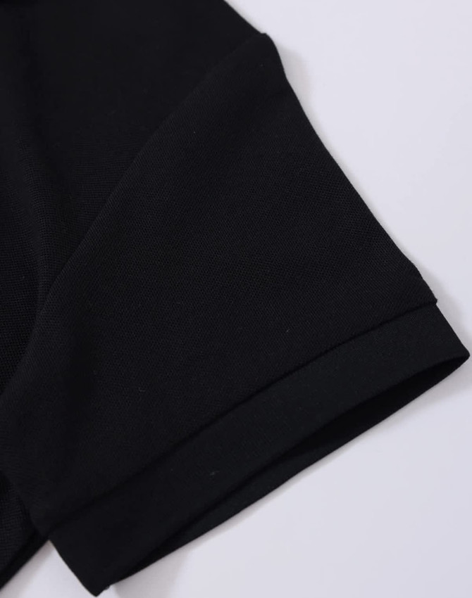 A close-up of a black polo shirt sleeve featuring a folded cuff and a subtle branding logo.