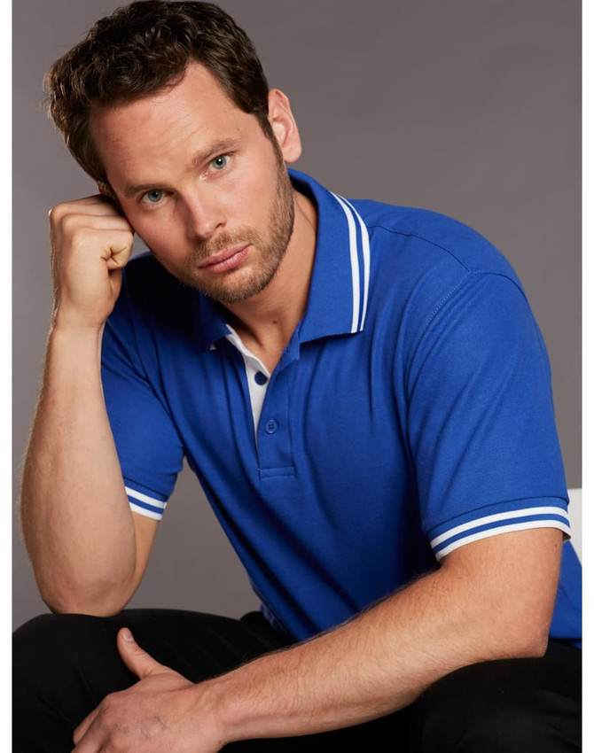A blue polo shirt featuring white detailing on the collar and sleeves, modelled by a man.