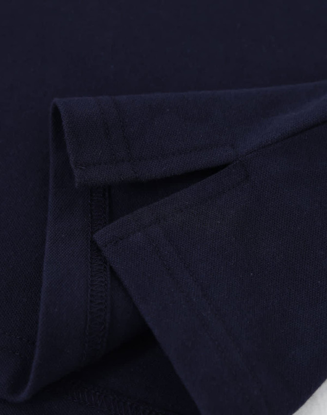 A close-up of a navy blue cotton stretch polo shirt, showcasing the fabric and folded sleeves. It features a logo.