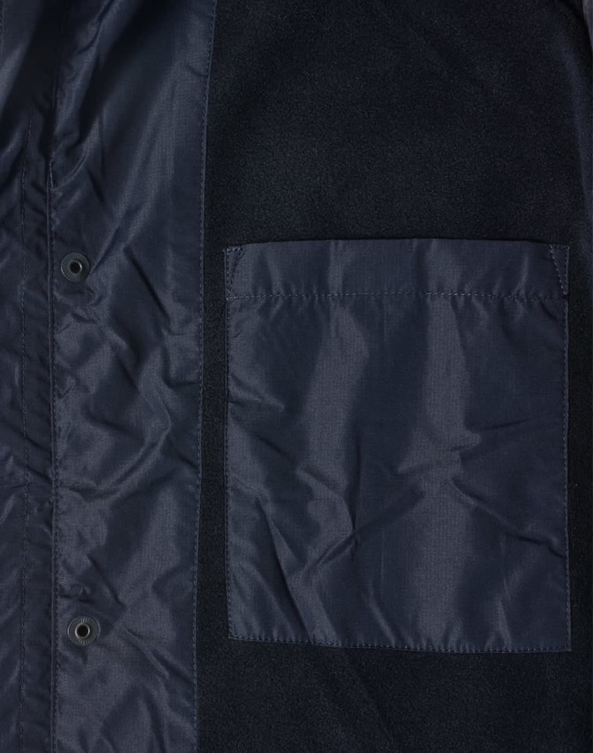A navy unisex jacket featuring a pocket and snap buttons, made from a mix of materials. It has a logo.