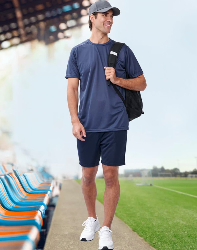 A man wearing a navy blue short-sleeve performance T-shirt and navy shorts, carrying a black backpack.