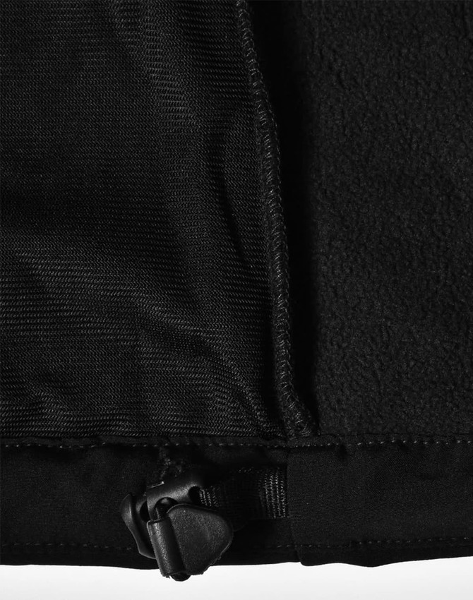 A close-up of a black softshell jacket featuring a zip and inner fleece lining, with a logo on the fabric.