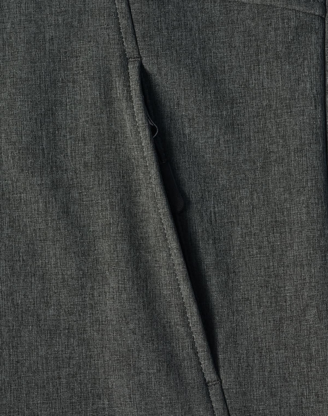 A close-up of a dark green softshell full zip hoodie featuring a zippered pocket and textured fabric.