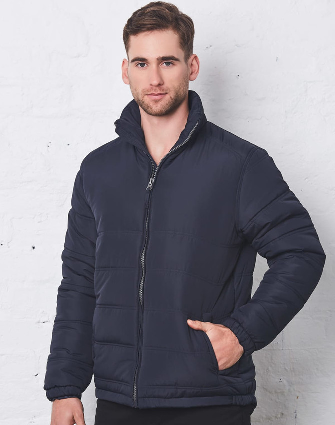 A navy heavy quilted puffer jacket with a zippered front and high collar, modelled by a man against a white wall.