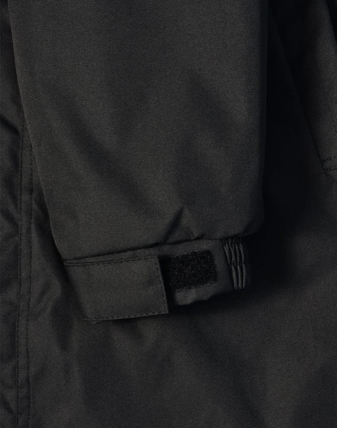 A close-up of a black long line stadium jacket featuring adjustable wrist cuffs and a logo.