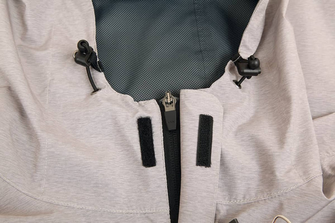 A close-up of a light grey waterproof performance jacket, featuring adjustable toggles and zip fastening.