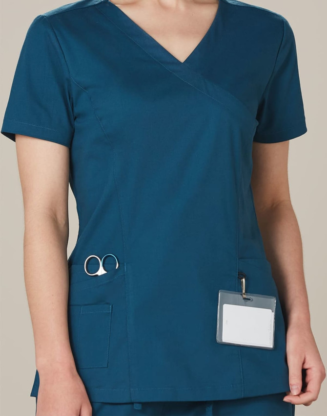 A solid colour teal scrub top with a V-neck, short sleeves, and pockets, featuring a logo on the pocket.