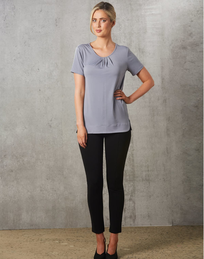 A grey short-sleeve knit top with pleats, paired with black fitted pants, worn by a model against a textured background.