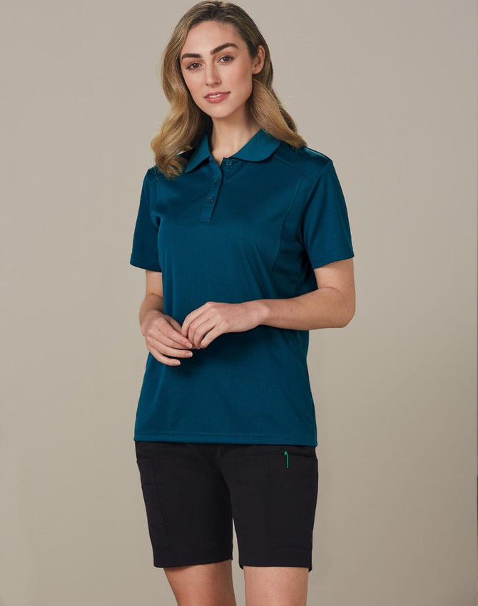 A model wearing dark cargo shorts and a teal polo shirt. The outfit includes a logo on the shirt.