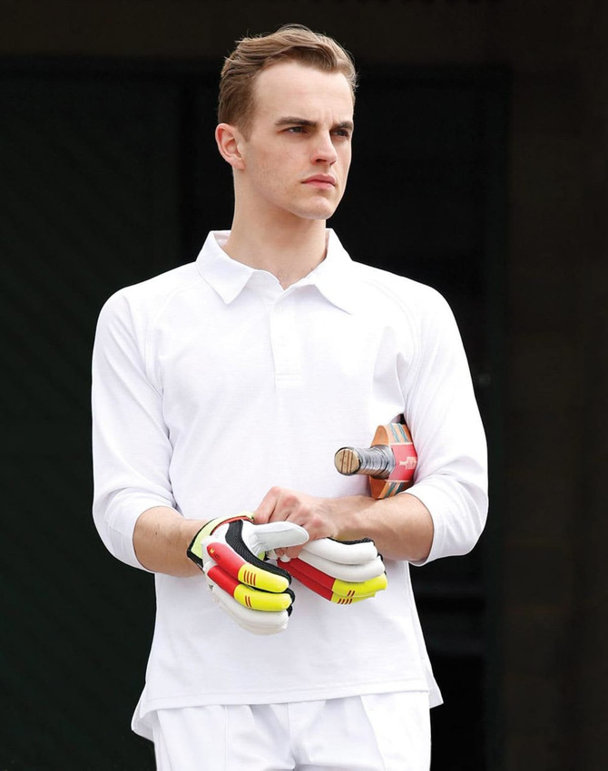 A white men's 3/4 sleeve cricket polo with a logo, worn by a model holding a cricket bat and gloves.
