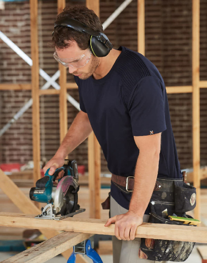 A navy blue short-sleeve work t-shirt worn by a man using a circular saw at a construction site.