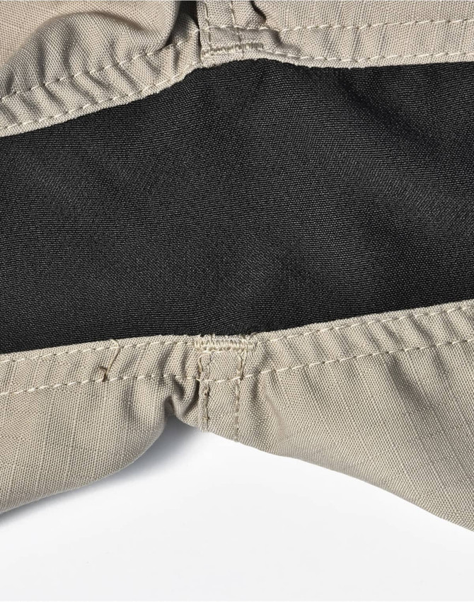 A close-up of beige work shorts featuring a black inner lining and stitched seams, with a logo visible.