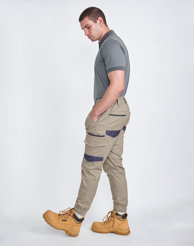 Unisex cotton stretch drill cuffed work pants in light beige with a logo, paired with a grey polo and yellow boots.