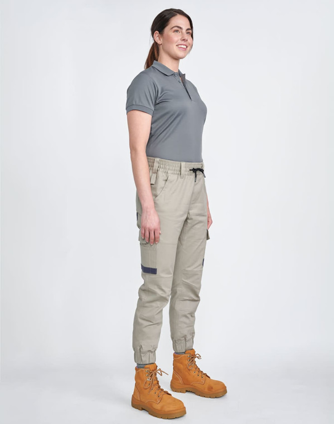Unisex cotton stretch drill cuffed work pants in khaki, paired with a grey polo and tan work boots. Features pockets and an elastic waistband.