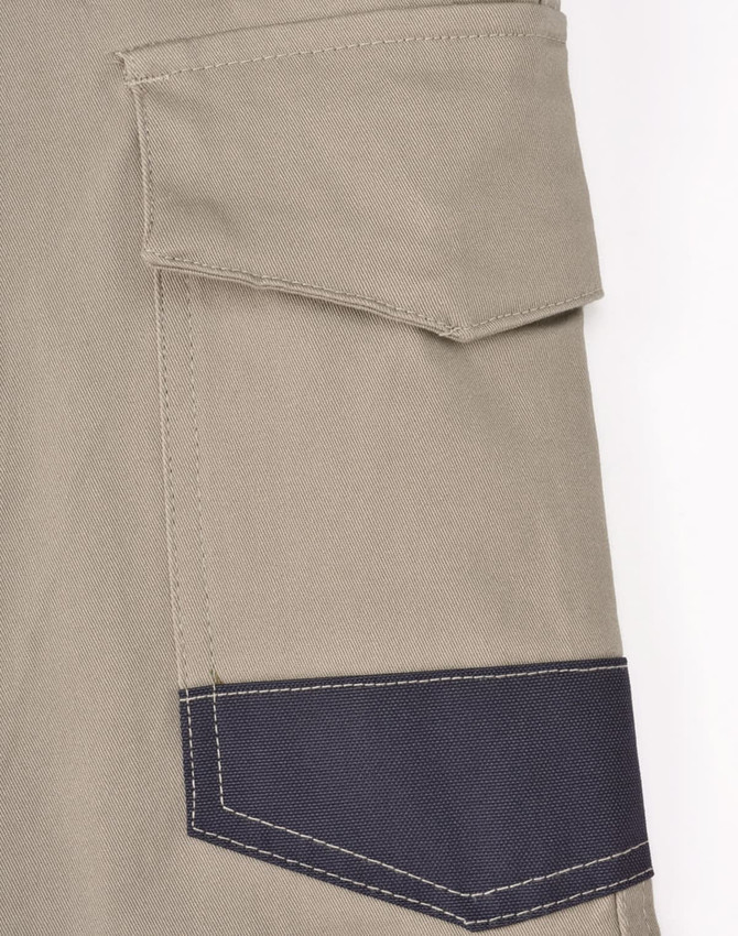 A close-up of unisex cotton stretch drill cuffed work pants in light khaki with a dark navy pocket detailing.