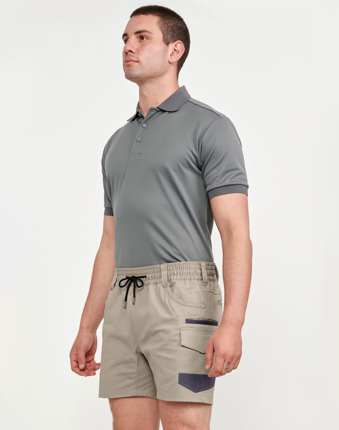 A man wearing a grey polo shirt and beige stretch drill work shorts with a logo. The shorts feature side pockets.