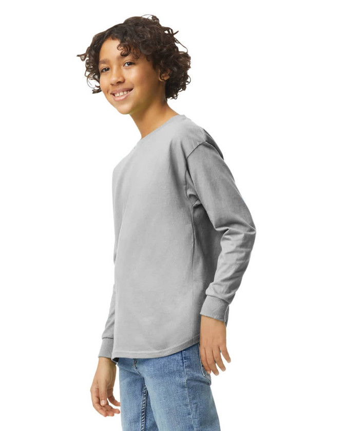 A youth long sleeve T-shirt in grey, featuring a logo, displayed on a model smiling at the camera.