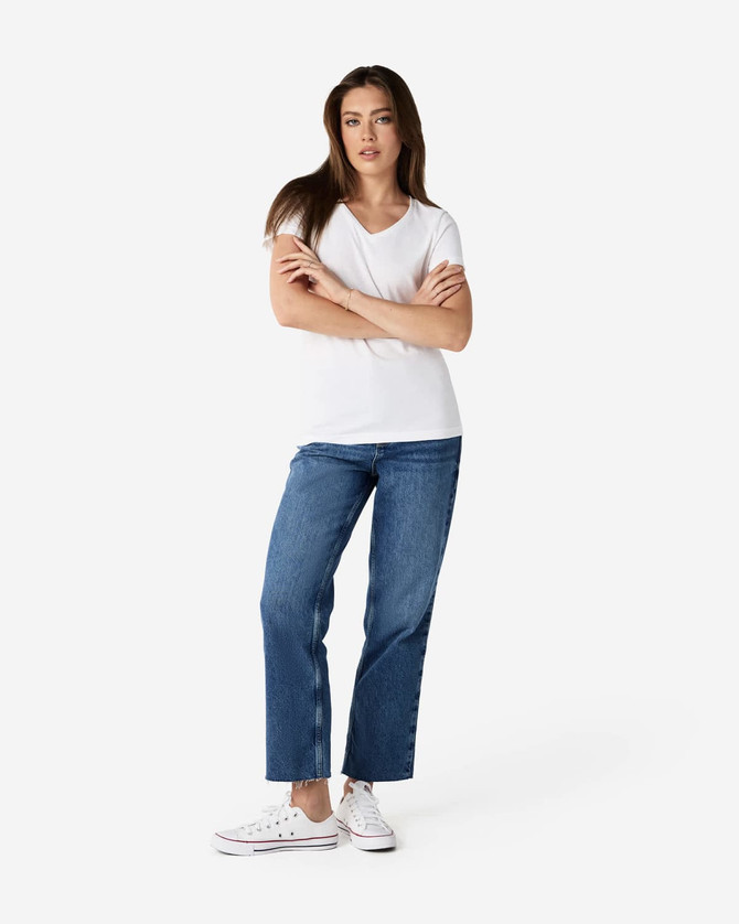 A model wearing a white Gildan Softstyle Ladies' V-Neck T-Shirt paired with blue jeans and white sneakers.