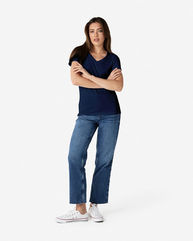 A woman is wearing a navy Gildan Softstyle ladies' V-neck T-shirt, paired with blue jeans and white sneakers.