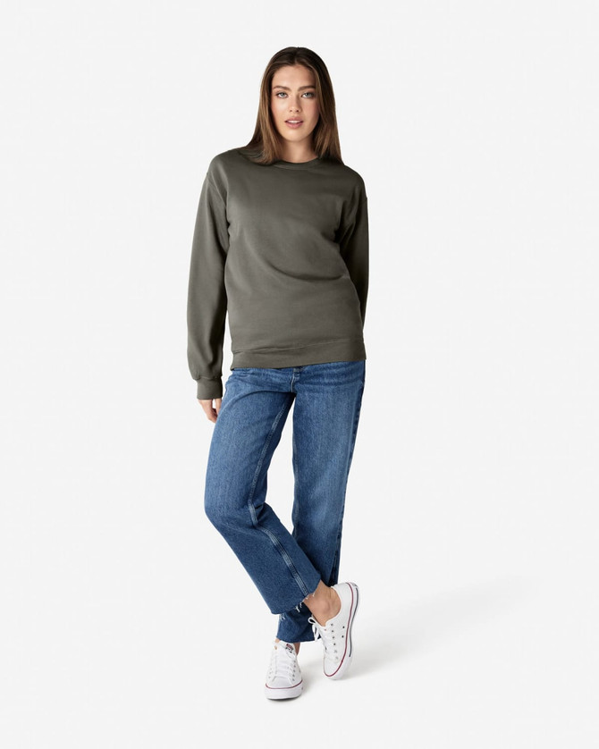 A woman wearing a dark green sweatshirt paired with blue jeans and white sneakers, standing casually.