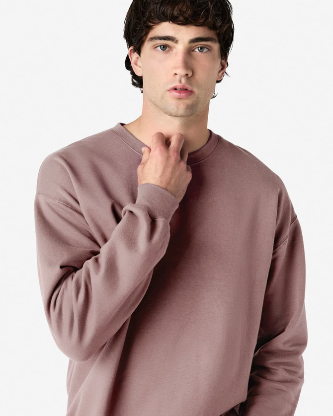 A model wearing a soft pink Gildan Softstyle adult sweatshirt. The sweatshirt features a classic fit and has a logo.