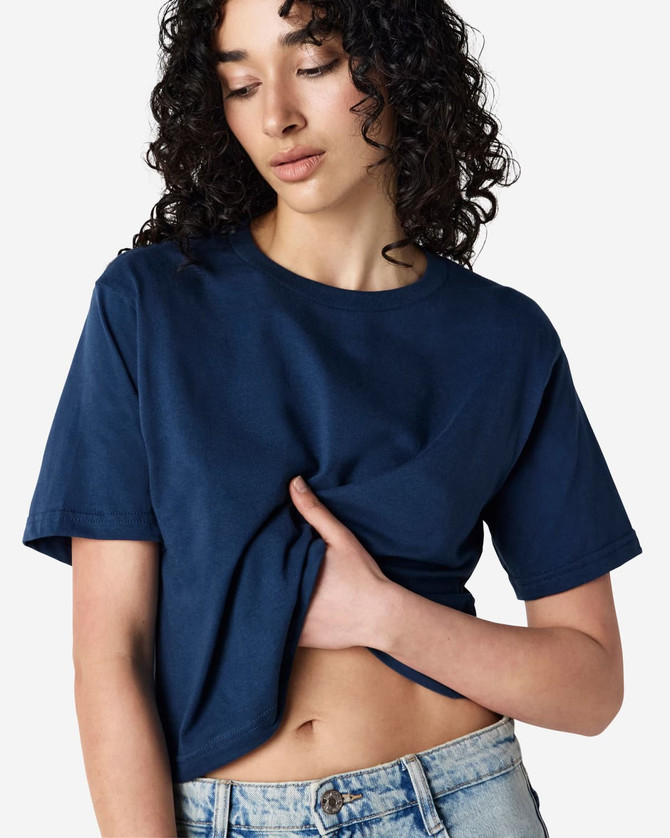 A navy blue boxy t-shirt with short sleeves, displayed on a model with curly hair. The shirt has a logo.