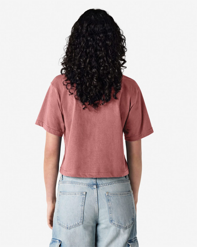 A woman with curly hair wearing a dusty rose boxy t-shirt, viewed from the back, with light blue cargo pants.