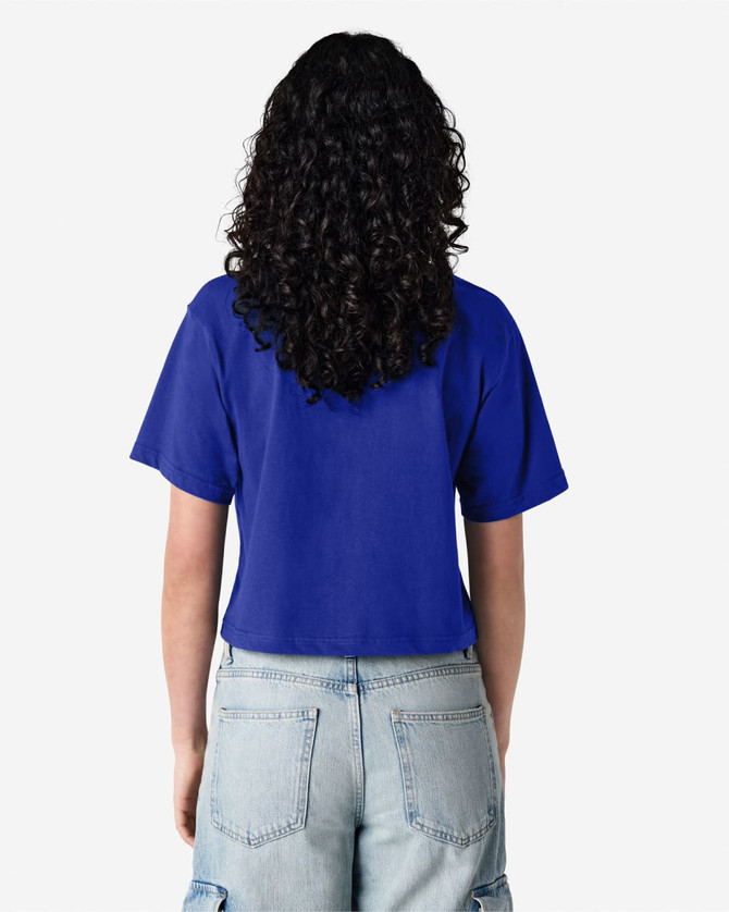A blue boxy t-shirt with short sleeves and a back view. The model wears high-waisted jeans and has curly hair.