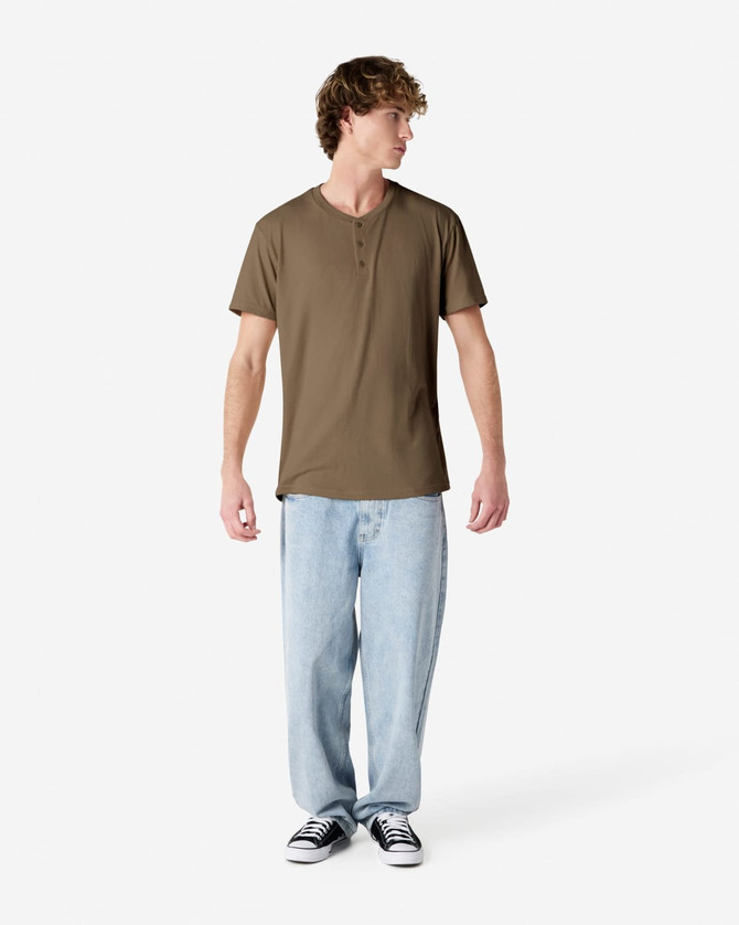 A unisex henley T-shirt in olive green, paired with light blue baggy jeans, displayed on a model.