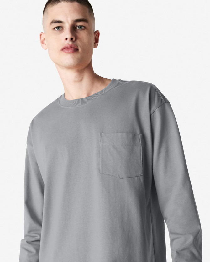 A model wearing a grey long-sleeve t-shirt with a pocket and a logo on the chest.